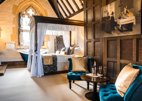 A bedroom with a four poster bed and teal armchair.